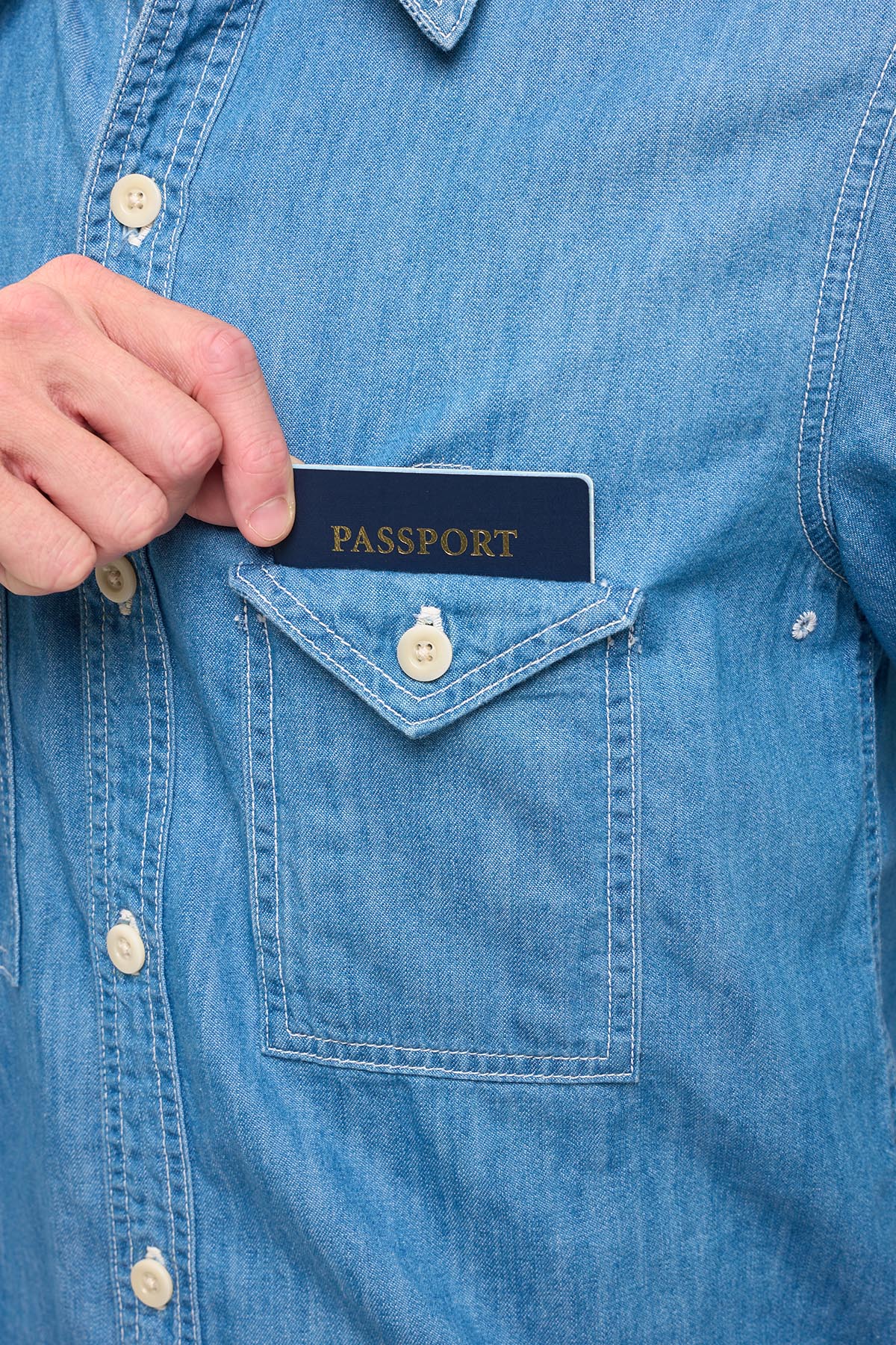 Hand placing a passport into the chech pocket of a blue chambray shirt.